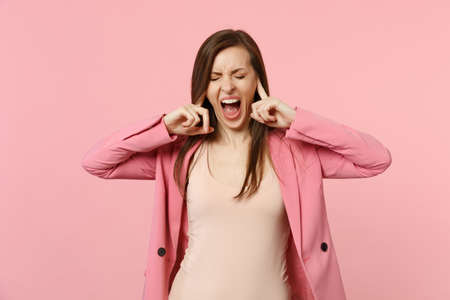 Crazy screaming young woman wearing jacket keeping eyes closed, covering ears with fingers isolated...