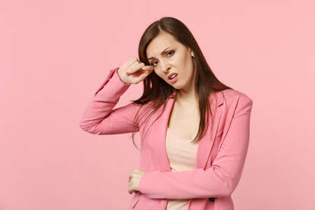 Portrait of exhausted crying young woman wearing jacket looking camera, wiping tears isolated on pastel pink wall background in studio. People sincere emotions, lifestyle concept. Mock up copy spaceの写真素材
