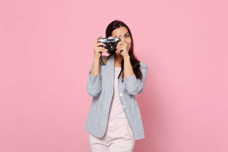 Portrait of pretty young woman in striped jacket taking pictures on retro vintage photo camera isolated on pink pastel wall background. People sincere emotions, lifestyle concept. Mock up copy spaceの写真素材