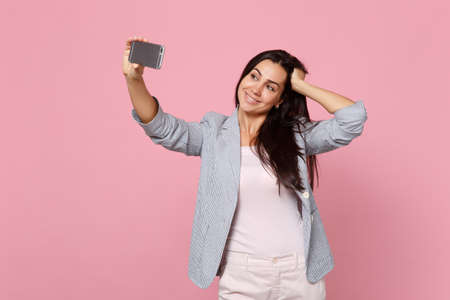 Charming young woman in striped jacket putting hand on head, doing selfie shot on mobile phone...