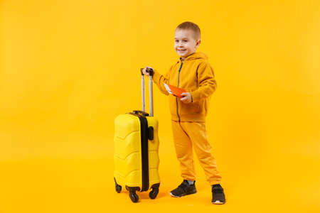 Little traveler tourist kid boy 3-4 years old isolated on yellow orange wall background studio. Passenger traveling abroad to travel on weekends getaway. Air flight journey concept. Mockup copy spaceの写真素材
