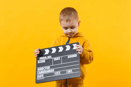 Little kid boy 3-4 years old in yellow clothes isolated on orange wall background, children studio portrait. People childhood lifestyle concept. Hand hold film making clapperboard. Mock up copy spaceの写真素材