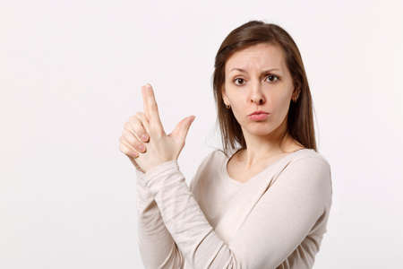 Portrait of puzzled pretty young woman in light clothes looking camera, holding hands like gun isolated on white background in studio. People sincere emotions, lifestyle concept. Mock up copy spaceの写真素材