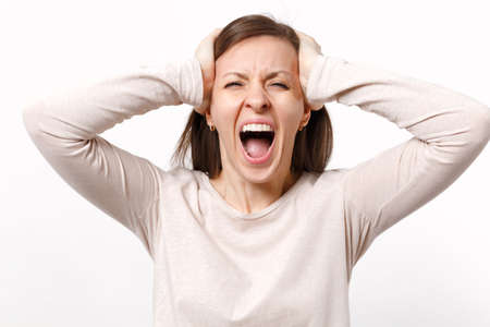 Portrait of crazy weird screaming young woman in light clothes putting hands on head isolated on...