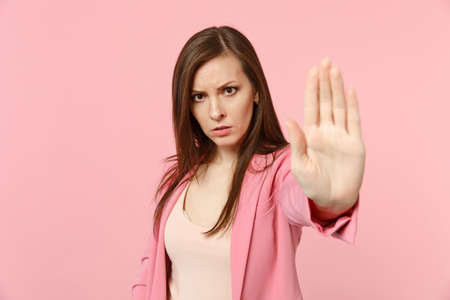 Portrait of disconcerted young woman in jacket looking camera, showing stop gesture with palm isolated on pastel pink wall background. People sincere emotions, lifestyle concept. Mock up copy spaceの写真素材