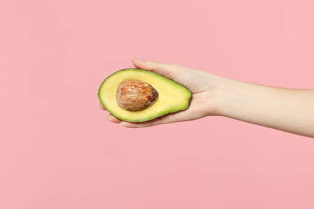 Close up cropped photo of female hold in hand fresh half green avocado fruit isolated on pink pastel wall background. Copy space advertising mock up. People vivid lifestyle, relax vacation conceptの写真素材
