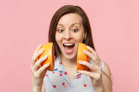 Excited young woman in summer clothes keeping mouth open hold halfs of fresh ripe grapefruit...