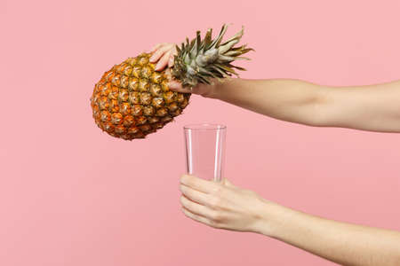 Close up cropped photo of female holding in hands fresh ripe pineapple fruit, glass cup isolated on pink pastel background in studio. People vivid lifestyle relax vacation concept. Mock up copy spaceの写真素材