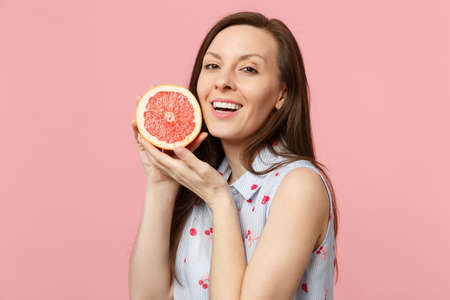 Beautiful young woman in summer clothes hold in hand half of fresh ripe grapefruit isolated on pink pastel wall background in studio. People vivid lifestyle relax vacation concept. Mock up copy spaceの写真素材