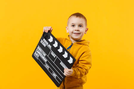 Little kid boy 3-4 years old in yellow clothes isolated on orange wall background, children studio portrait. People childhood lifestyle concept. Hand hold film making clapperboard. Mock up copy spaceの写真素材