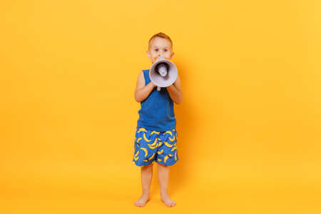 Kid boy 3-4 years old in blue beach summer clothes hold speak in megaphone isolated on bright yellow orange background children studio portrait. People childhood lifestyle concept Mock up copy spaceの写真素材
