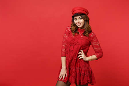 Portrait of smiling charming young woman in lace dress, cap standing, looking camera isolated on bright red wall background in studio. People sincere emotions lifestyle concept. Mock up copy spaceの写真素材