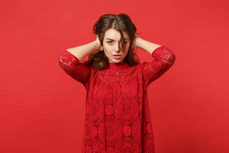 Portrait of beautiful young woman in lace dress looking camera, putting hands on head isolated on bright red wall background in studio. People sincere emotions, lifestyle concept. Mock up copy spaceの写真素材