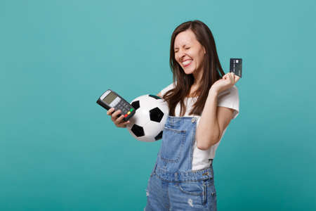 Overjoyed pretty young woman football fan support favorite team with soccer ball, wireless modern bank payment terminal to process, acquire credit card payments isolated on blue turquoise backgroundの写真素材