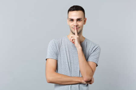 Portrait of attractive young man in casual clothes saying hush be quiet with finger on lips shhh...