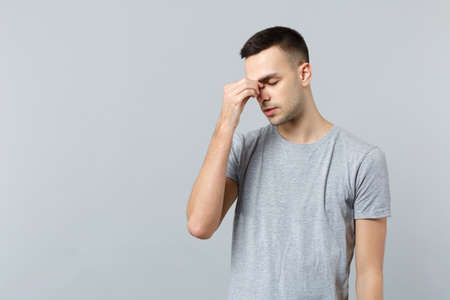 Portrait of exhausted young man in casual clothes keeping eyes closed, putting hand on nose isolated on grey wall background in studio. People sincere emotions, lifestyle concept. Mock up copy spaceの写真素材