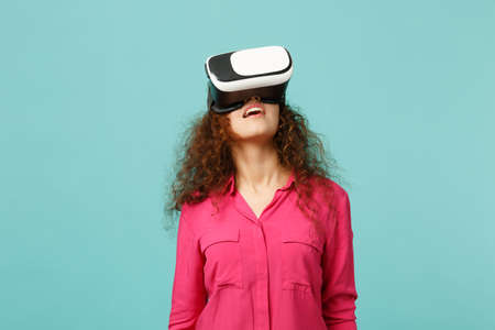 Portrait of young african girl in pink casual clothes looking up in headset isolated on blue...