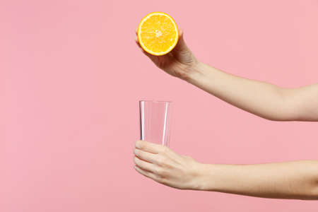 Close up cropped photo of female holding in hands half of fresh ripe orange fruit, glass cup isolated on pink pastel wall background. People vivid lifestyle relax vacation concept. Mock up copy spaceの写真素材