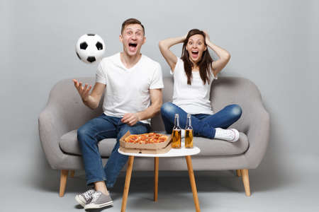 Excited screaming couple woman man football fans in white t-shirt cheer up support favorite team with soccer ball isolated on grey background. People emotions, sport family leisure lifestyle conceptの写真素材