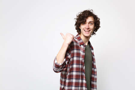Portrait of cheerful young man in casual clothes looking camera, pointing thumb aside behind his back isolated on white wall background. People sincere emotions, lifestyle concept. Mock up copy spaceの写真素材