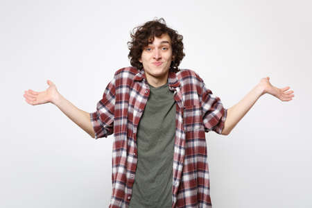 Portrait of perplexed smiling young man in casual clothes looking camera and spreading hands isolated on white wall background in studio. People sincere emotions lifestyle concept. Mock up copy spaceの写真素材