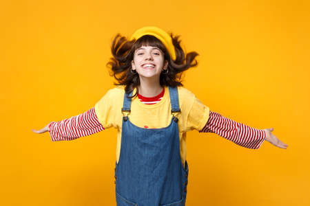 Portrait of cheerful girl teenager in french beret jumping with flowing hair spreading hands isolated on yellow background in studio. People sincere emotions, lifestyle concept. Mock up copy spaceの写真素材