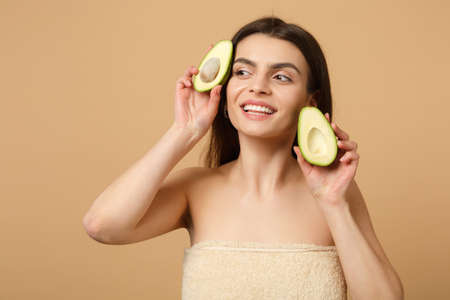 Close up brunette half naked woman 20s with perfect skin nude make up hold avocado isolated on beige pastel wall background studio portrait. Healthcare cosmetic procedures concept. Mock up copy spaceの写真素材