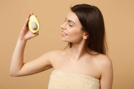 Close up brunette half naked woman 20s with perfect skin nude make up hold avocado isolated on beige...
