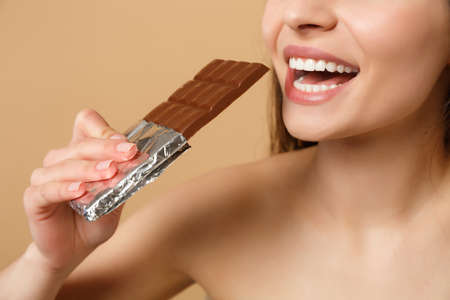Close up half naked woman 20s with perfect skin, nude make up hold chocolate bar isolated on beige pastel wall background, studio portrait. Health care cosmetic procedures concept. Mock up copy spaceの写真素材