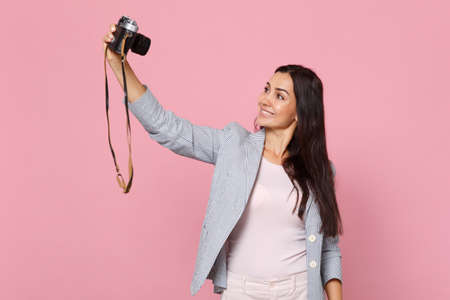 Portrait of smiling young woman in striped jacket doing selfie shot on retro vintage photo camera isolated on pink pastel wall background. People sincere emotion lifestyle concept. Mock up copy spaceの写真素材