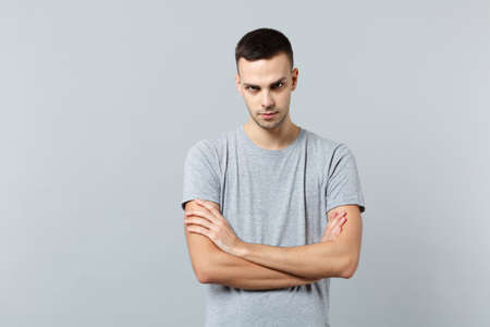 Portrait of angry strict young man in casual clothes looking camera, holding hands crossed isolated on grey wall background in studio. People sincere emotions, lifestyle concept. Mock up copy spaceの写真素材