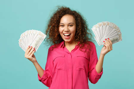 Joyful african girl in casual clothes holding fan of money in dollar banknotes, cash money isolated...