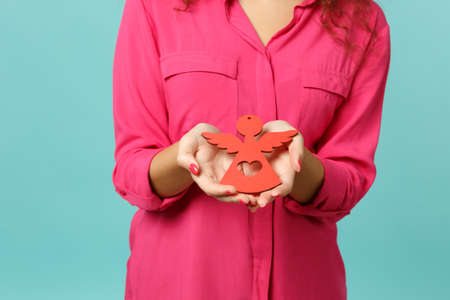 Cropped image of young woman in casual clothes holding wooden decorative toy angel isolated on blue turquoise wall background in studio. People sincere emotions, lifestyle concept. Mock up copy spaceの写真素材