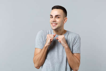 Portrait of smiling joyful young man in casual clothes looking camera and clenching fists isolated...