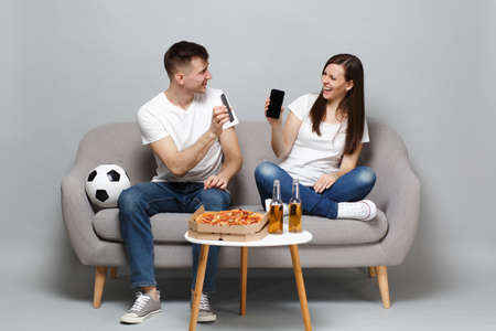Laughing couple woman man football fans cheer up support favorite team holding mobile phone with blank empty screen isolated on grey background. People emotions sport family leisure lifestyle conceptの写真素材