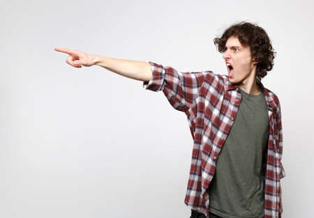 Portrait of angry screaming young man in casual clothes swearing, looking pointing index finger...