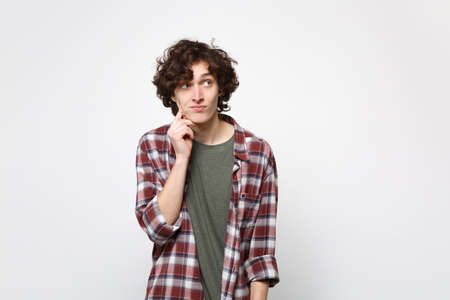 Portrait of pensive young man in casual clothes looking aside, put hand prop up on chin isolated on white wall background in studio. People sincere emotions, lifestyle concept. Mock up copy spaceの写真素材
