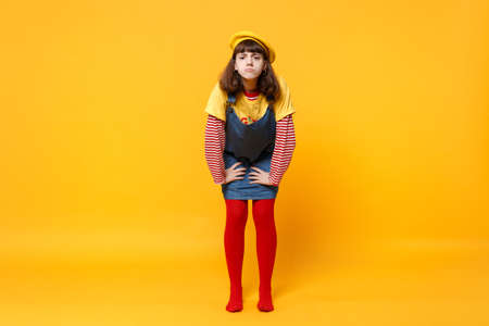 Full length portrait of dissatisfied girl teenager in french beret denim sundress standing isolated...