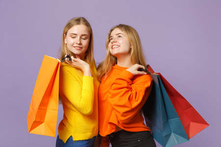 Two pensive young blonde twins sisters girls in vivid clothes holding package bag with purchases...