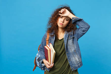 Young sad african american girl teen student in denim clothes, backpack hold books isolated on blue background studio portrait. Education in high school university college concept. Mock up copy spaceの写真素材