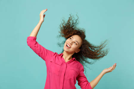 Portrait of laughing pretty african girl in casual clothes jumping with flying hair isolated on blue turquoise wall background in studio. People sincere emotions lifestyle concept. Mock up copy spaceの写真素材