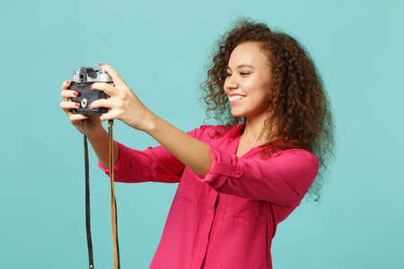 Pretty african girl in casual clothes doing selfie shot on retro vintage photo camera isolated on...