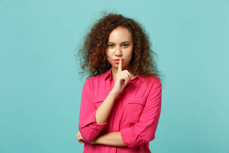 Attractive african girl in casual clothes saying hush be quiet with finger on lips shhh gesture isolated on blue turquoise background. People sincere emotions lifestyle concept. Mock up copy spaceの写真素材