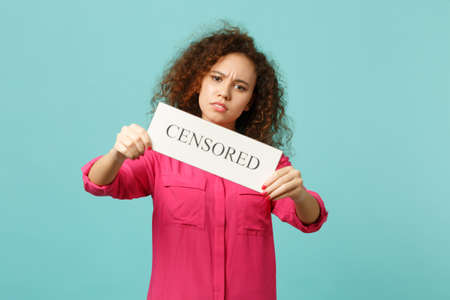Portrait of bewildered african girl in pink casual clothes hold text board CENSORED isolated on blue...