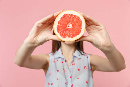 Young woman in summer clothes holding, covering face with half of fresh ripe grapefruit isolated on pink pastel background in studio. People vivid lifestyle relax vacation concept. Mock up copy spaceの写真素材
