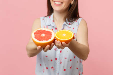 Cropped image of young woman in summer clothes hold halfs of fresh ripe grapefruit, orange fruit isolated on pink pastel background. People vivid lifestyle relax vacation concept. Mock up copy spaceの写真素材