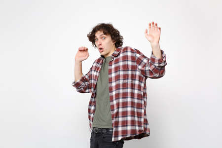 Portrait of shocked scared young man in casual clothes looking camera, rising hands showing palms...