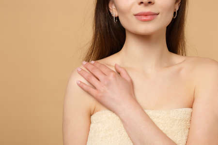 Close up brunette half naked woman with perfect skin hand on shoulder isolated on beige pastel wall background studio portrait. Skin care healthcare cosmetic procedures concept. Mock up copy spaceの写真素材