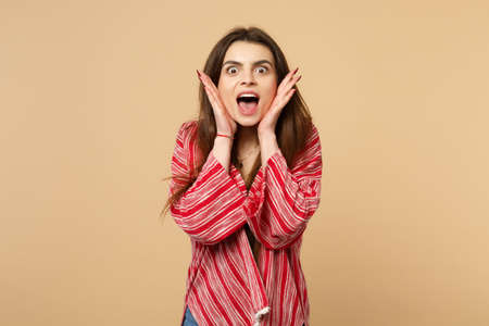 Portrait of amazed young woman in casual clothes keeping mouth wide open putting hand on cheeks...
