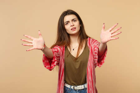 Portrait of displeased young woman in casual clothes standing with outstretched hands isolated on pastel beige wall background in studio. People sincere emotions lifestyle concept. Mock up copy spaceの写真素材